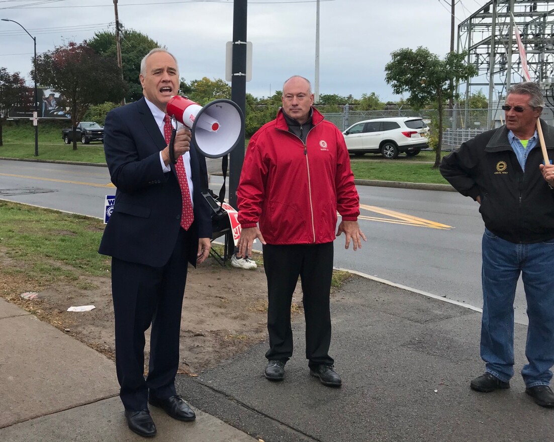 New York State Comptroller Tom DiNapoli speaks into a megaphone next to UAW Local 1097 President Dan Maloney.